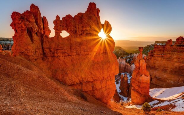 Red rock formations in Utah with sun shining through a natural arch at sunrise