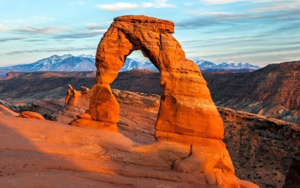 The famous Utah natural rock formation known as Delicate Arch with snow capped mountains in the background