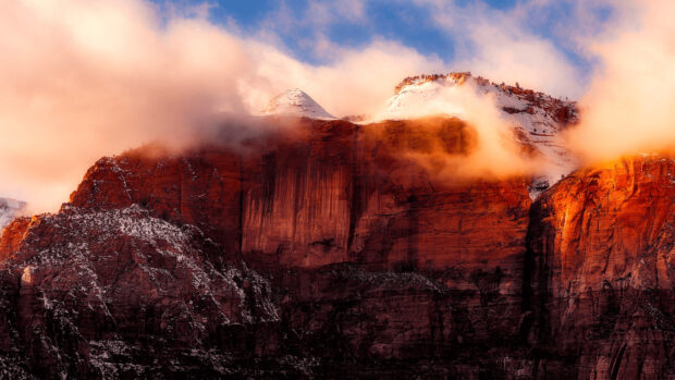 Snow capped Utah cliffs glowing orange under mist and blue sky