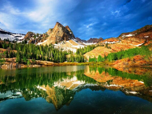 The Utah mountain range reflected in a calm lake surrounded by dense forest and rocky terrain