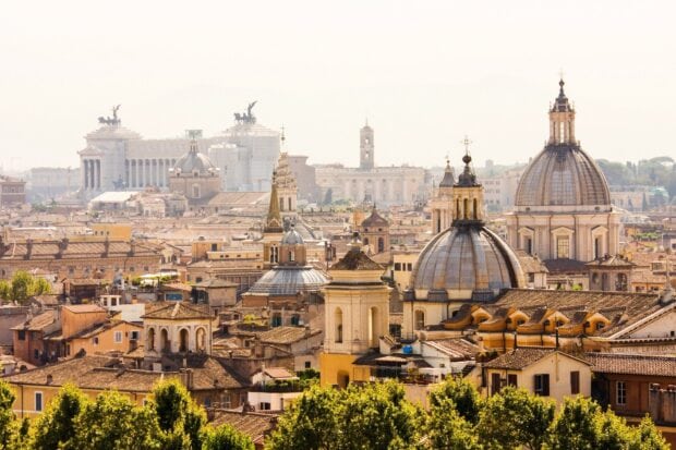 A panoramic view of Vatican City rooftops and historic domes in warm sunlight