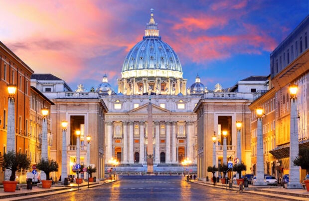 The Vatican City with an illuminated dome under a colorful sunset sky