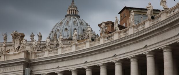 The dome and statues of Vatican City architecture under a cloudy sky