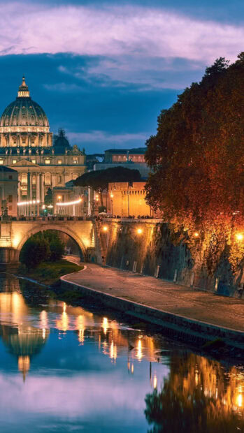 Illuminated Vatican City dome and riverside path reflecting lights at dusk