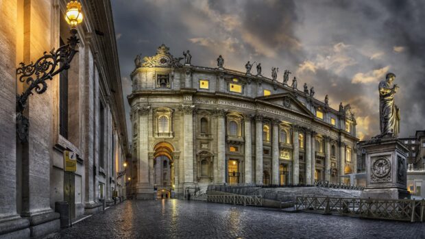 The architecture of Vatican City with statues and illuminated columns at dusk