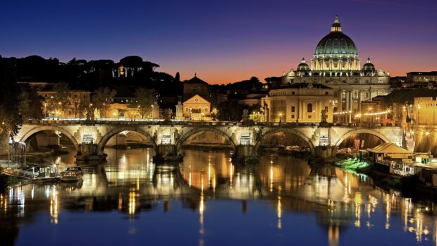 Vatican City scenic architecture with illuminated dome and bridge over reflective river at dusk