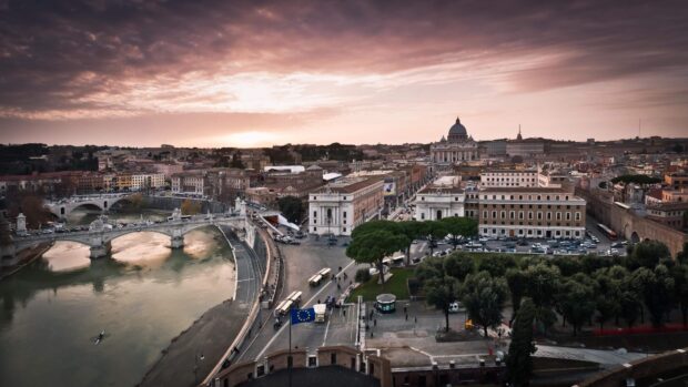 A panoramic view of Vatican City with historic buildings and the river under a cloudy sunset sky
