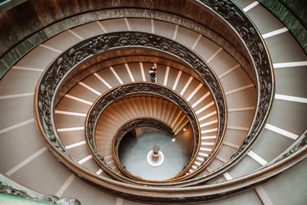 A man standing on the spiral staircase inside Vatican City with detailed decorative railings