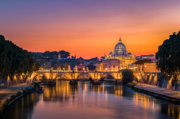 Sunset view of Vatican City with the dome and illuminated bridge over the river