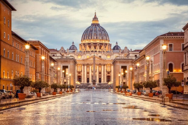 The architecture of Vatican City with illuminated street lamps and wet pavement at dusk