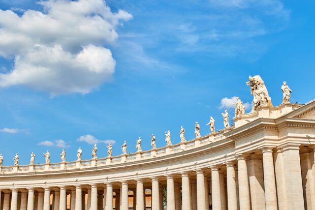 The colonnade with statues in Vatican City under a bright blue sky