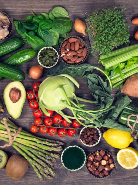 Fresh vegetables including kale, asparagus, avocado, and tomatoes on a wooden table