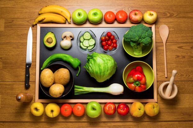 Fresh vegetables including lettuce broccoli and peppers arranged on a wooden table with a knife and chopping board