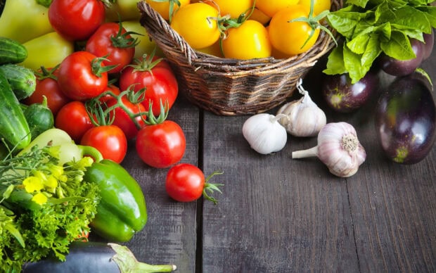 Fresh vegetables including tomatoes bell peppers garlic and eggplants on a wooden table