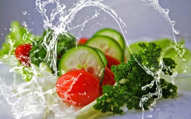 Fresh cucumber tomato and parsley vegetables with splashing water on white surface