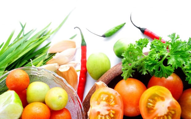 Fresh vegetables including tomato garlic chili and herbs on a white surface