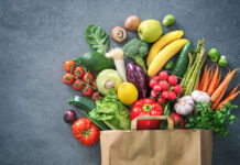 Fresh vegetables spilling out of a paper bag on a stone surface with avocado broccoli and carrots