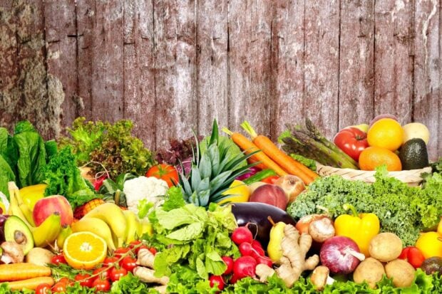 A variety of fresh vegetables including carrots lettuce eggplant and radishes arranged in front of a rustic wooden background