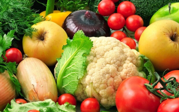 A variety of fresh vegetables including cauliflower tomatoes onions and leafy greens on display