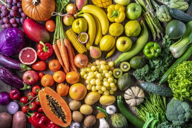 A colorful assortment of vegetables displayed on a wooden surface including carrots corn and bell peppers