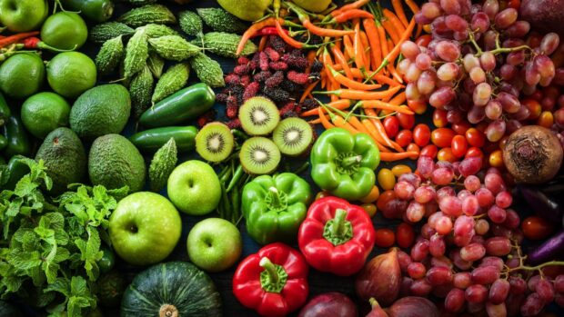 Fresh vegetables assortment including bell peppers and kiwi fruit displayed on dark surface