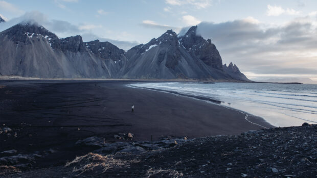 A person standing on the black sand beach with Vestrahorn Iceland mountain range in the background