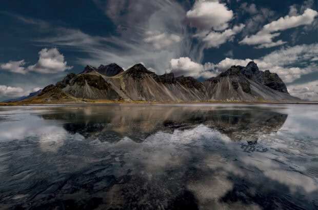 Dramatic clouds over rocky Vestrahorn Iceland mountain range reflected in calm water