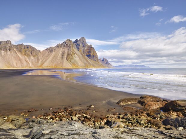 Rocky coastline and black sand beach at Vestrahorn Iceland with towering mountains in the background