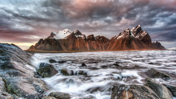 Rocky coastline with Vestrahorn Iceland mountains in the background and waves crashing on the shore