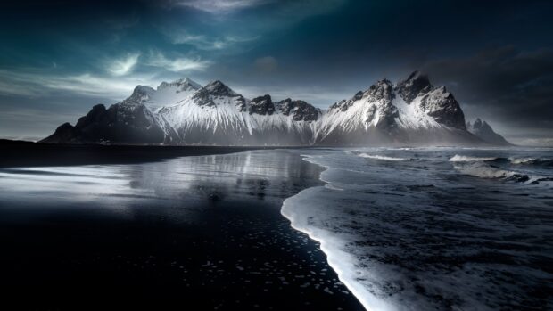 Snow covered Vestrahorn Iceland mountain range with dark beach and ocean waves