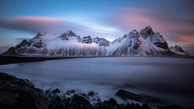 Snow covered Vestrahorn Iceland mountain with rocky foreground and calm sea during sunrise