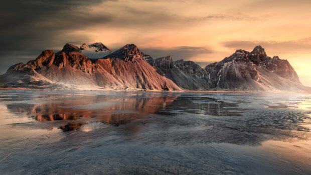 Vestrahorn Iceland features dramatic mountain peaks reflected in calm water at sunset