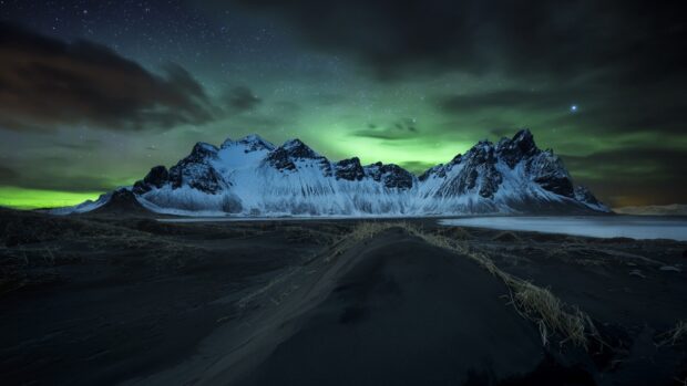 Snow covered Vestrahorn Iceland mountain range under green northern lights and starry night sky