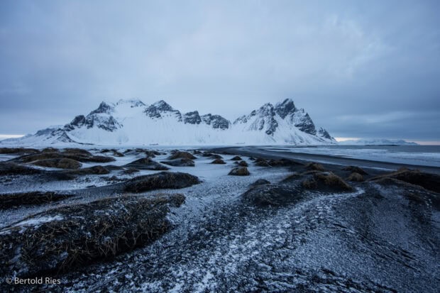 Snow covered Vestrahorn Iceland landscape with icy black sand dunes under cloudy sky