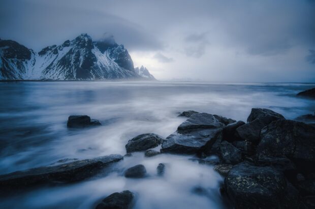 Snow covered Vestrahorn Iceland mountain with rocks and mist over the sea shore