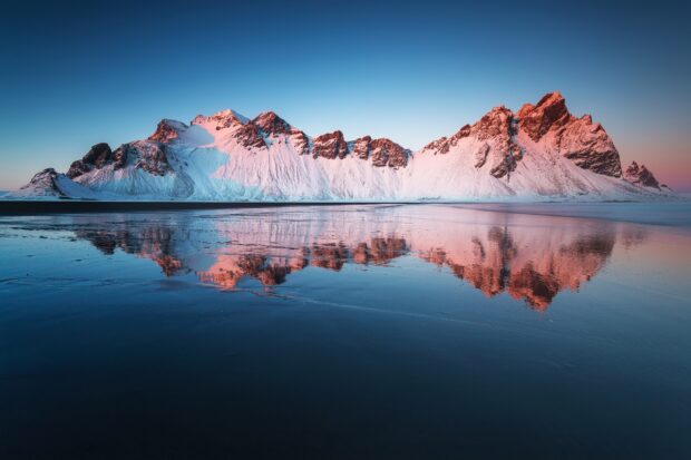 Snow covered Vestrahorn Iceland mountain range reflecting on calm water during sunset with clear sky