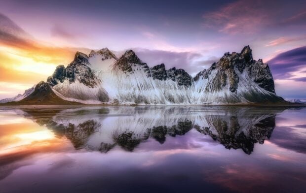 Snowy mountain range at Vestrahorn Iceland reflecting on calm water during sunset