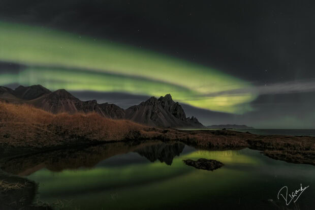 The Vestrahorn Iceland mountain range under the northern lights reflected in the still water