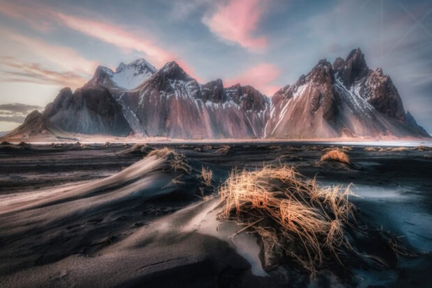 Vestrahorn Iceland with black sand dunes and dry grass under a colorful sunrise sky