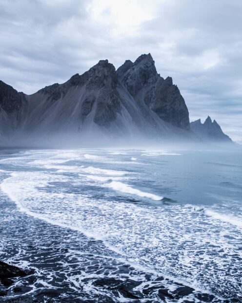 Mist surrounds Vestrahorn Iceland mountain range with waves crashing on the shore
