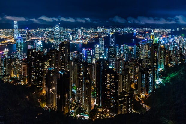 A vibrant cityscape view at night from Victoria Peak showcasing illuminated skyscrapers and harbor lights
