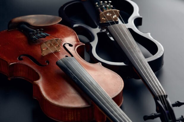 A close up of two violas placed side by side on a dark surface showing detailed strings and wood grain
