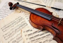 A wooden viola resting on old sheet music showcasing classic musical notes and vintage pages