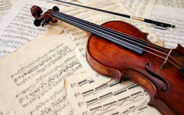 A wooden viola resting on old sheet music showcasing classic musical notes and vintage pages