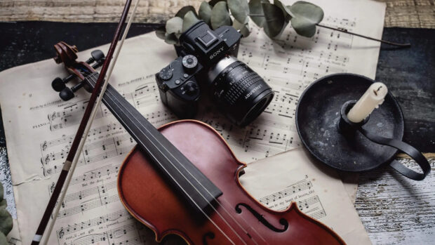 A classic viola resting on sheet music with a camera and vintage candle holder nearby