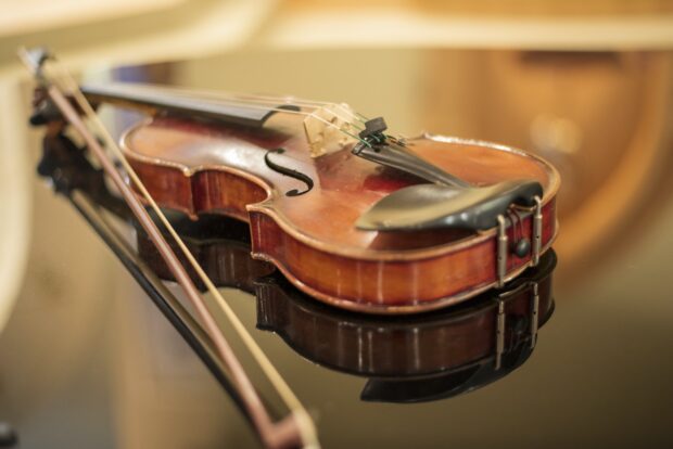 A close up of a wooden viola resting on a reflective surface with a bow nearby