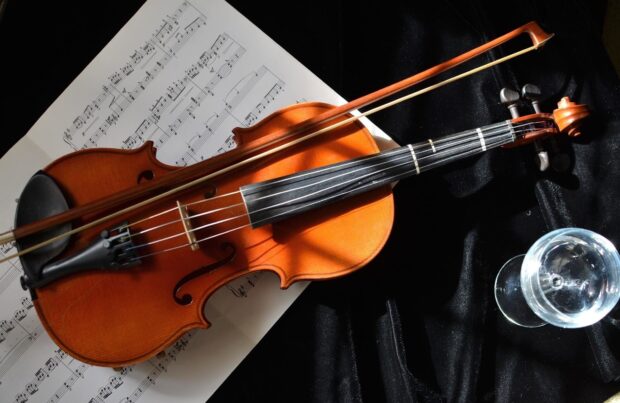 A wooden viola resting on sheet music with a glass of water nearby on black fabric