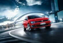 Red Volkswagen Lamando GTS driving fast on city road under bridge at dusk