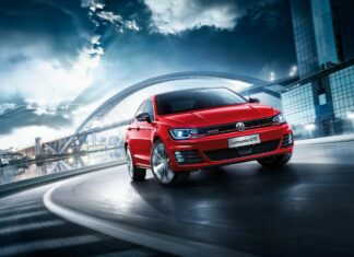 Red Volkswagen Lamando GTS driving fast on city road under bridge at dusk