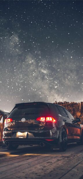 Black Volkswagen parked under a starry night sky with glowing red taillights